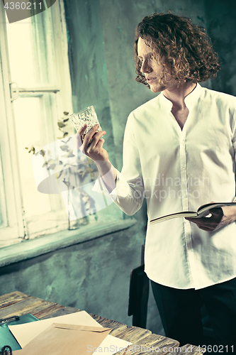 Image of Writer at work. Handsome young writer standing near the table and making up something in his mind