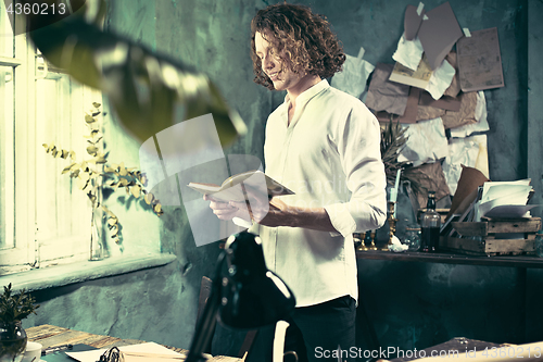 Image of Writer at work. Handsome young writer standing near the table and making up something in his mind