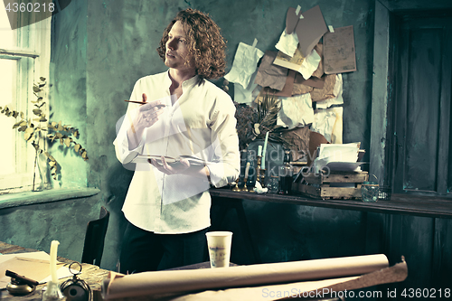 Image of Writer at work. Handsome young writer standing near the table and making up something in his mind