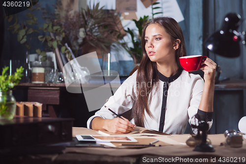 Image of Young beautiful woman working with cup of coffee