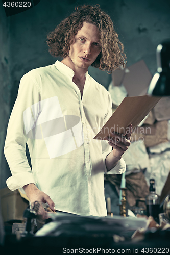 Image of Writer at work. Handsome young writer standing near the table and making up something in his mind