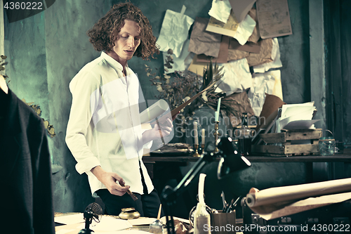 Image of Writer at work. Handsome young writer standing near the table and making up something in his mind