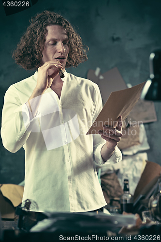 Image of Writer at work. Handsome young writer standing near the table and making up something in his mind