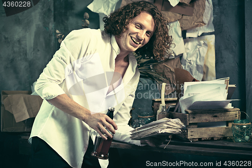 Image of Writer at work. Handsome young writer standing near the table and making up something in his mind