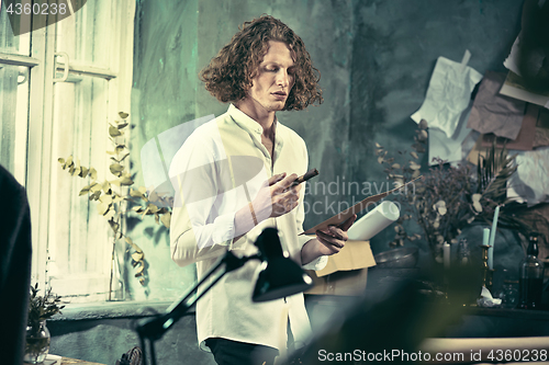 Image of Writer at work. Handsome young writer standing near the table and making up something in his mind