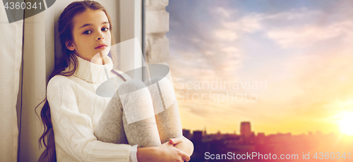 Image of sad girl sitting on sill at home window