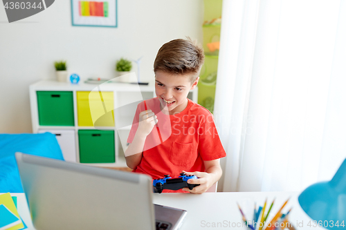 Image of boy with gamepad playing video game on laptop