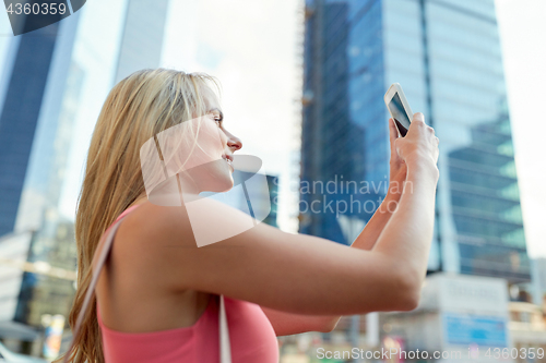 Image of young woman with smartphone photographing city