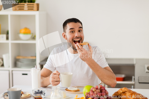 Image of man eating toast with coffee at home kitchen