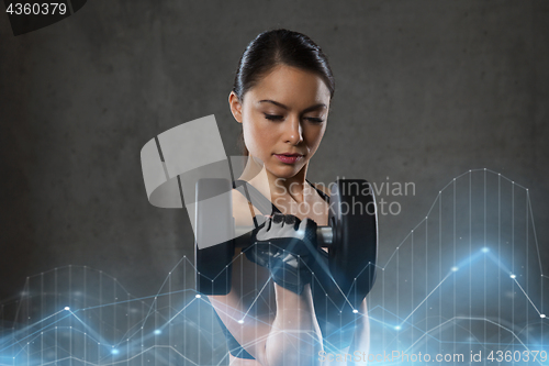 Image of young woman flexing muscles with dumbbells in gym