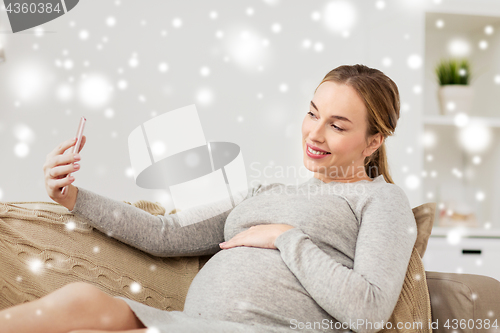 Image of pregnant woman taking smartphone selfie at home