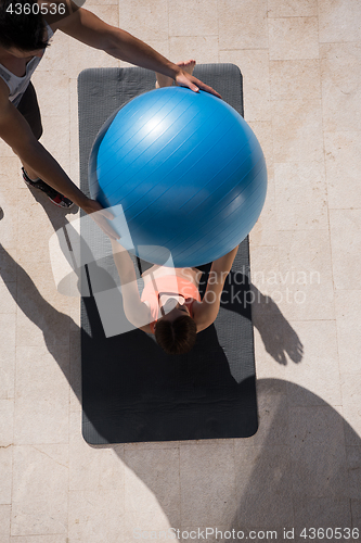 Image of woman and personal trainer doing exercise with pilates ball