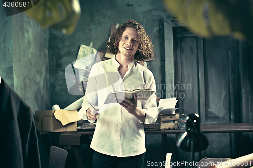 Image of Writer at work. Handsome young writer standing near the table and making up something in his mind