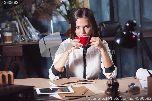 Image of Young beautiful woman working with cup of coffee