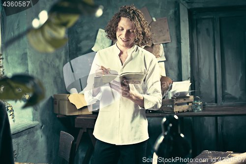 Image of Writer at work. Handsome young writer standing near the table and making up something in his mind