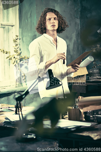 Image of Writer at work. Handsome young writer standing near the table and making up something in his mind