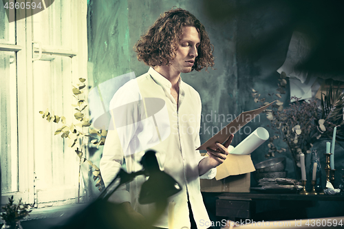 Image of Writer at work. Handsome young writer standing near the table and making up something in his mind