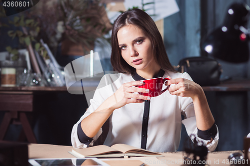 Image of Young beautiful woman working with cup of coffee