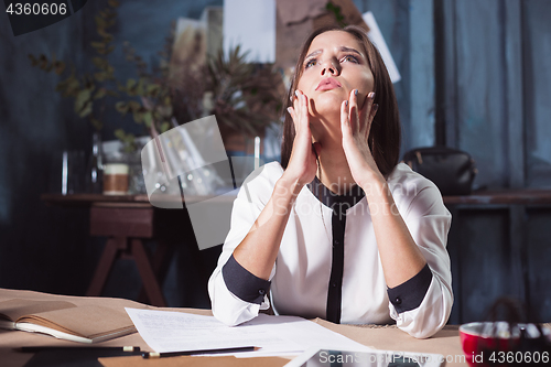 Image of Young frustrated woman working at office desk in front of laptop