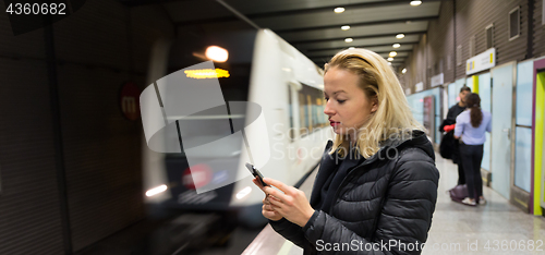 Image of Woman with a cell phone waiting for metro.