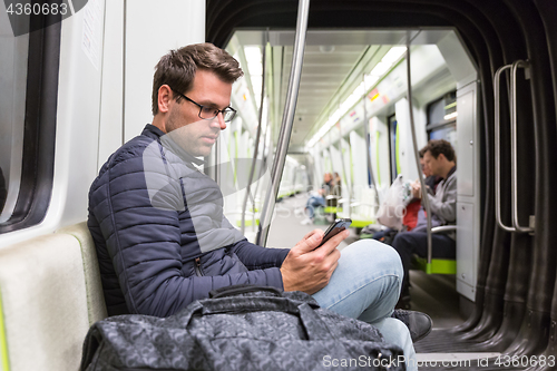 Image of Male commuter reading from mobile phone screen in metro.