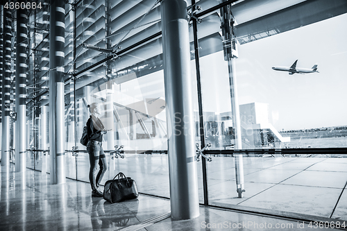 Image of Young woman waiting at airport, looking through the gate window.