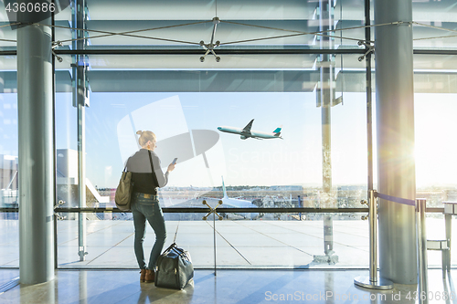 Image of Young woman waiting at airport, looking through the gate window.