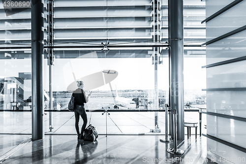 Image of Young woman waiting at airport, looking through the gate window.