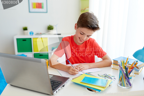 Image of student boy with laptop writing to notebook