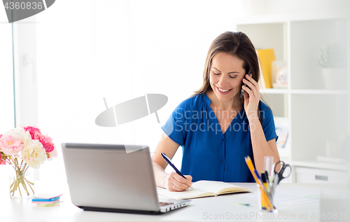 Image of woman with notepad calling on smartphone at office