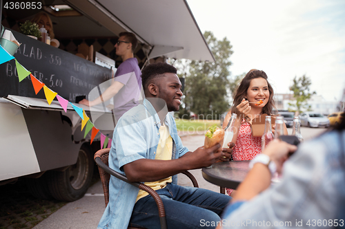 Image of happy friends with drinks eating at food truck