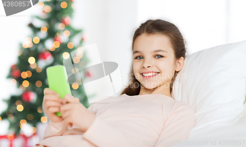 Image of happy girl in bed with smartphone at christmas