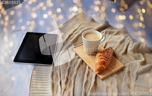 Image of tablet pc, coffee and croissant on bed at home