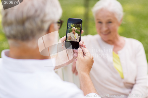 Image of old woman photographing man by smartphone in park