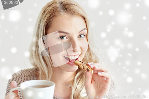 Image of happy woman with tea eating cookie in winter