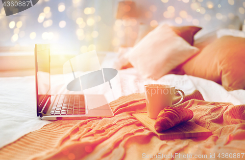 Image of laptop, coffee and croissant on bed at cozy home