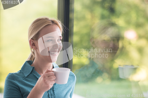 Image of young woman drinking morning coffee by the window