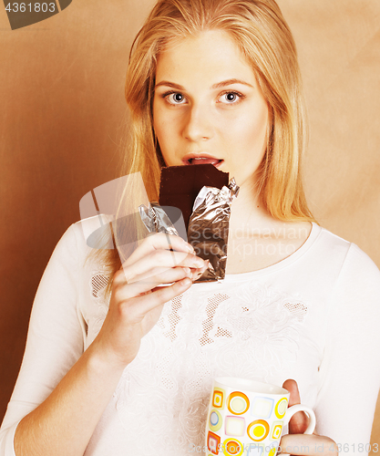 Image of young cute blond girl eating chocolate and drinking coffee close