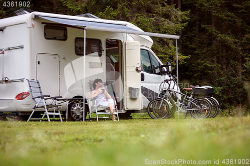 Image of Woman is standing with a mug of coffee near the camper RV.