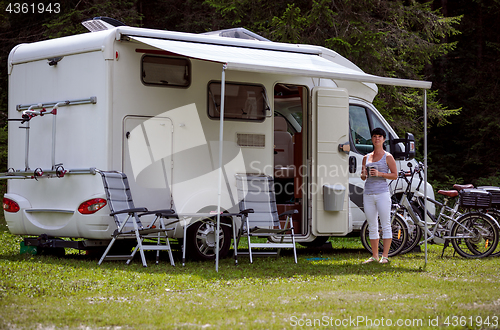 Image of Woman is standing with a mug of coffee near the camper RV.