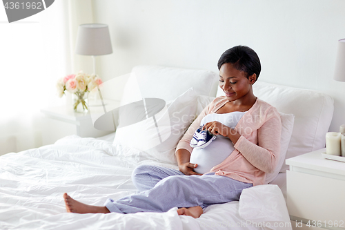 Image of pregnant african woman with baby bootees in bed