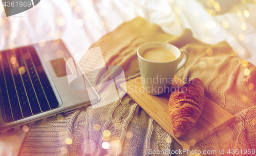 Image of laptop, coffee and croissant on bed at cozy home