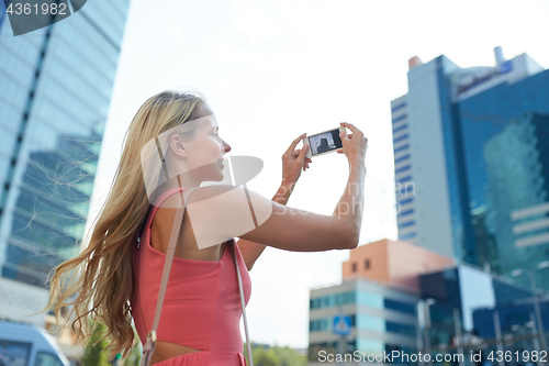 Image of young woman with smartphone photographing city