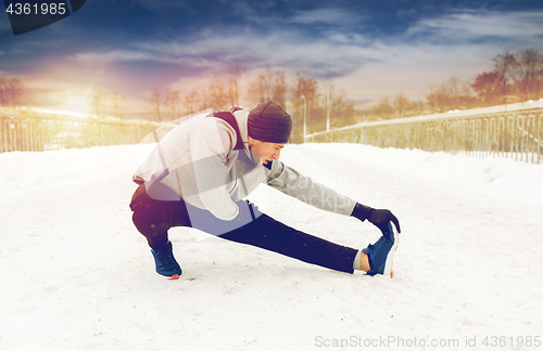 Image of man exercising and stretching leg on winter bridge