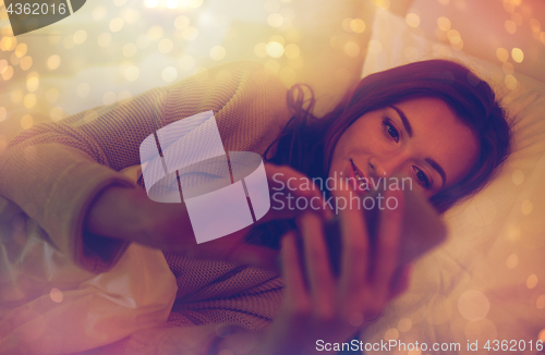 Image of young woman with smartphone in bed at home bedroom