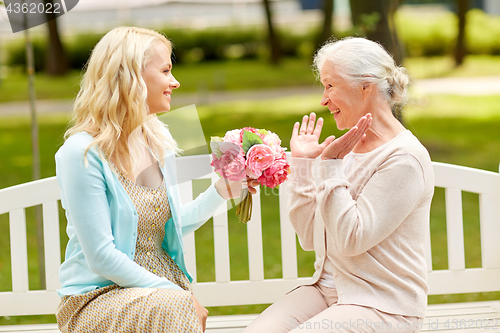 Image of daughter giving flowers to senior mother at park