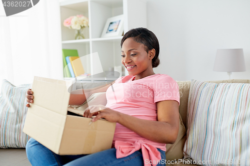 Image of happy pregnant woman opening parcel box at home