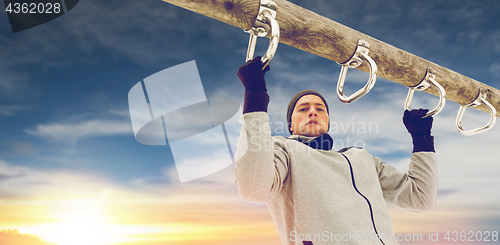 Image of young man exercising on horizontal bar in winter