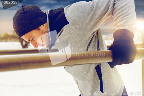 Image of young man exercising on parallel bars in winter