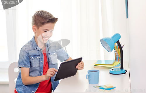 Image of smiling boy with tablet pc sitting at home desk